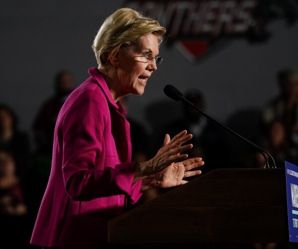 warren in a pink blazer speaking at a podium