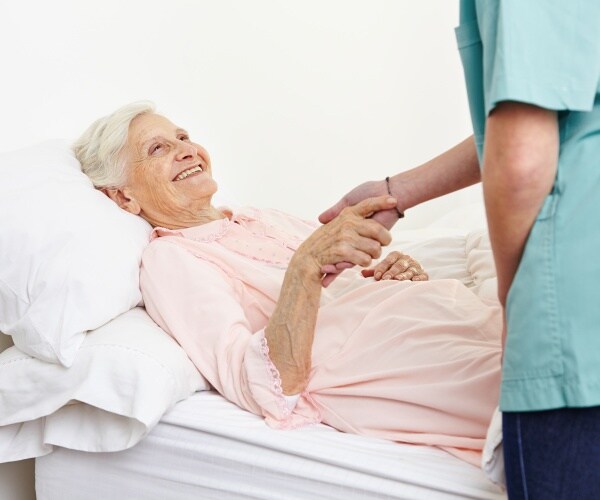 older woman in hospice, laying on bed and smiling while shaking hand of hospice worker