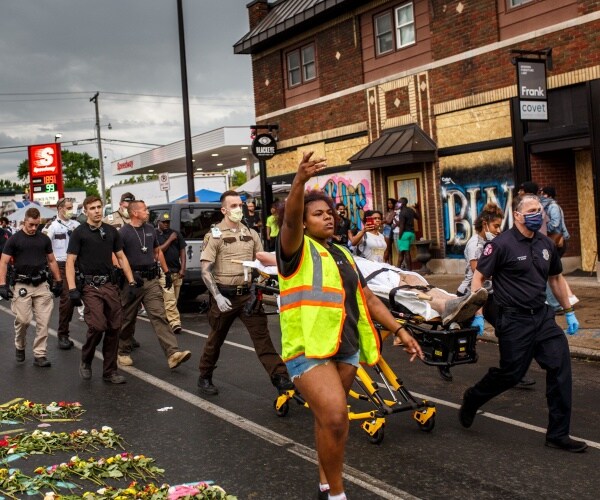 police and paramedic in a yellow vest carry a protester who fainted in the road