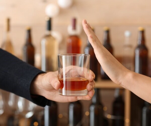 person holding out booze in glass and other person putting a hand up to say 'no' to it