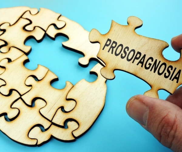 hand holding puzzle piece with prosopagnosia written on it, putting in place in puzzle of a brain