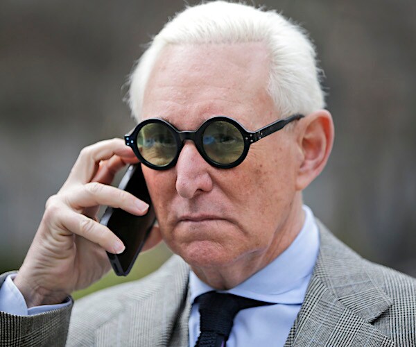 roger stone wearing sunglasses and holding a cell phone to his right ear