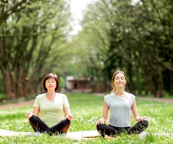 younger and older woman doing yoga outside on summer day