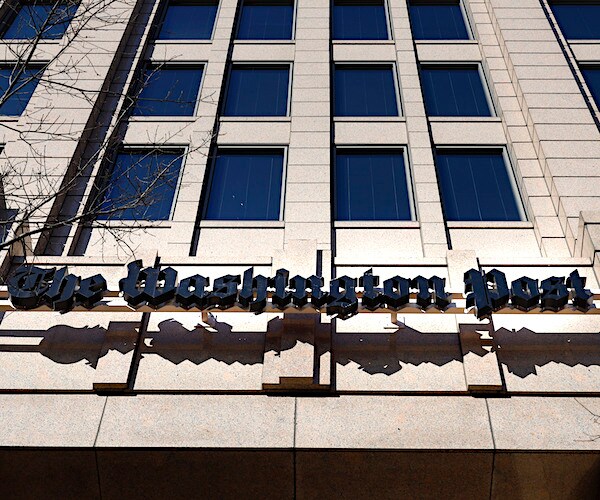 the washington post building is shown from the street view looking up the front side of the building with its sign above