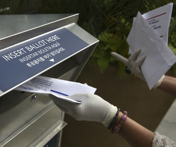 A woman wearing gloves drops off a mail-in ballot at a drop box in Hackensack, N.J