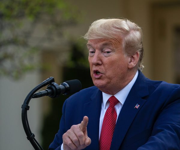 president trump stands at a podium outside and speaks into microphone