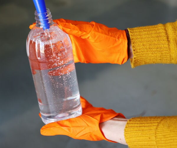 a person wearing orange safety gloves holds a bottle of hand sanitizer 