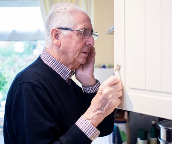 older man looking forgetful as he looks in cabinet