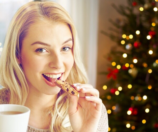 woman eating a cookie with coffee in front of Christmas tree