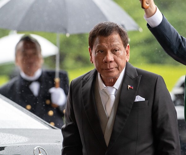 rodrio duerte walks from a car with an umbrella held over his head