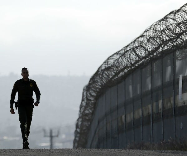 a border patrol agent walks along the border fence