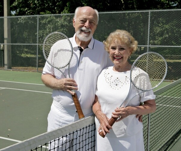 an older man and woman holding tennis rackets at court