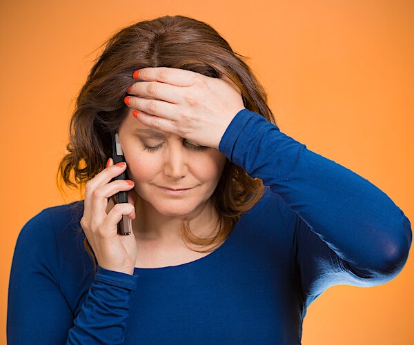 a distressed woman holds her forehead while she holds a smart phone up to her right ear