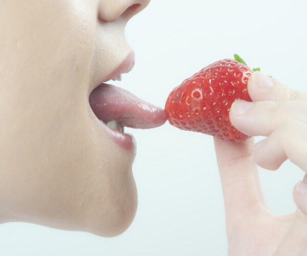 Closeup of woman's tongue out tasting a strawberry