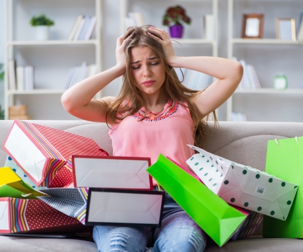 woman looking anxious sitting on couch with lots of gifts after shopping spress