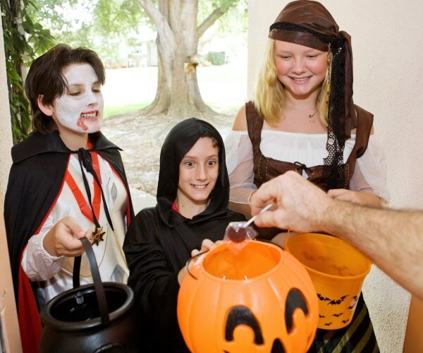 trick-or-treaters at a door, woman handing out lollipops