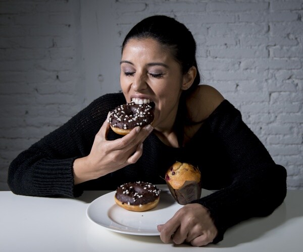 woman with a plate of donuts, biting into one chocolate donut