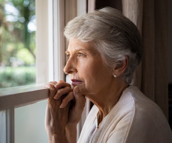 older woman looking out window, looking lonely