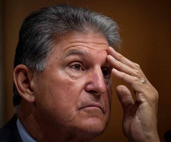 joe manchin sits in hearing with head resting on hand