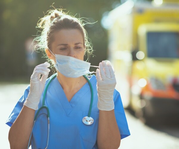 female physician looking tired and sad taking off her mask outside of hospital