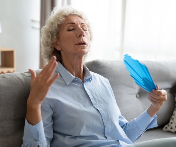 older woman fanning herself in living room because hot