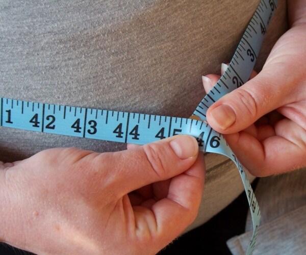 close up of woman measuring waist with measuring tape