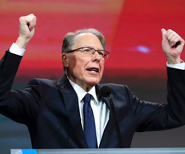 wayne lapierre lifts both arms above his head during an national rifle association speech