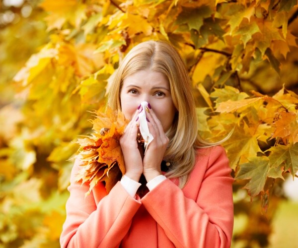 woman blowing nose with fall foliage behind her