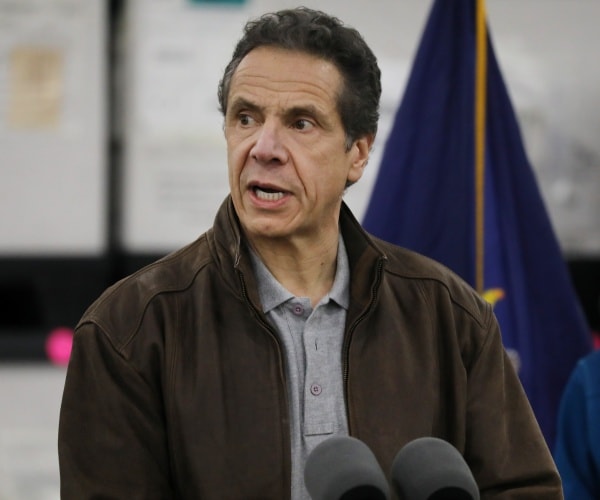 cuomo in a gray polo shirt and brown jacket sitting outside