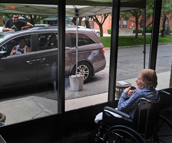 an elderly woman in a nursing home is visited, by car, by her family