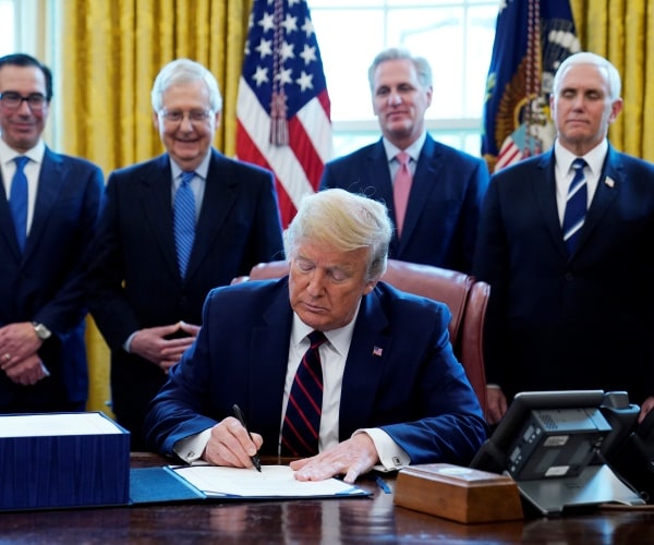 trump signs paper in a navy suit while mcconnell, mccarthy, mnuchin, and pence stand behind him 