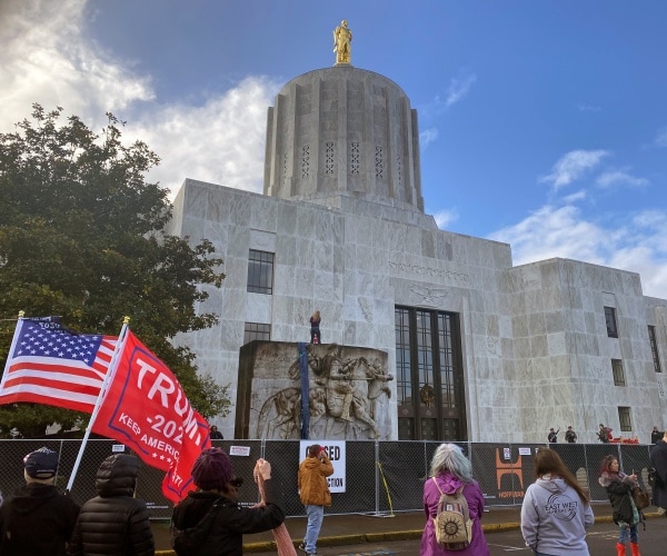 protesters hold trump 2020 signs and a flag outside the oregon state capitol.