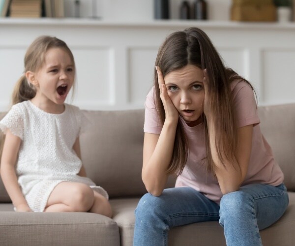 little girl having a tantrum on couch with frustrated mother next to her