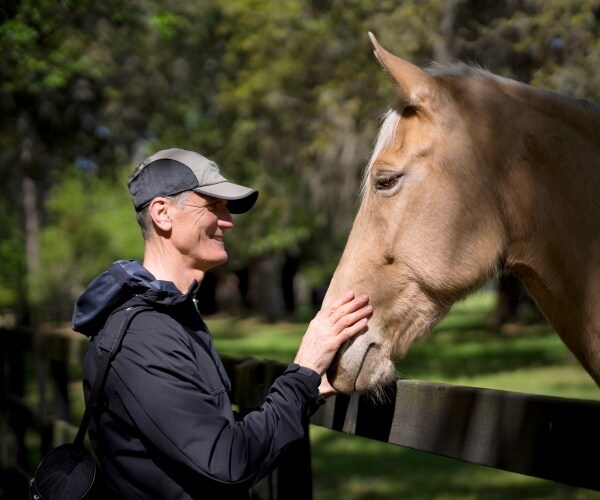 an older man smiling and petting a horse