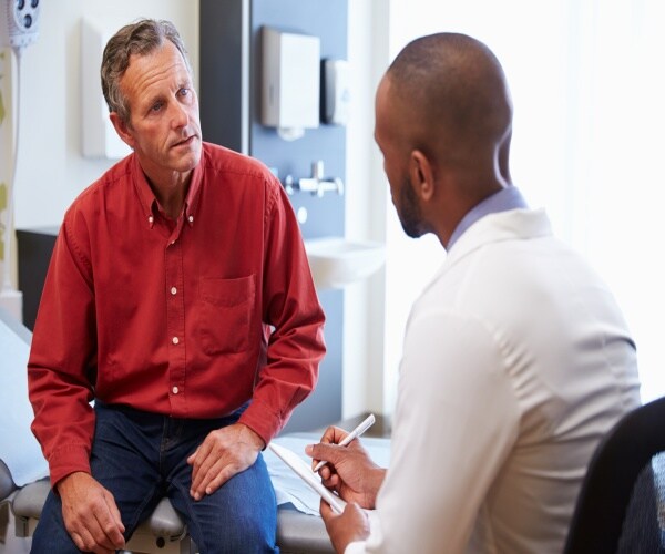 Male patient talking to doctor while doctor takes notes in hospital room