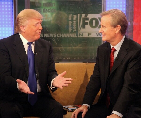 trump in a black suit and blue tie sits down next to doocy in a black suit and red tie