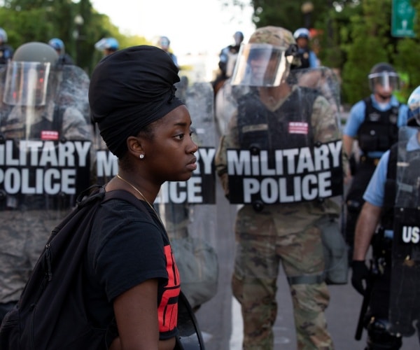 military police wearing camouflage uniforms as a protester walks by