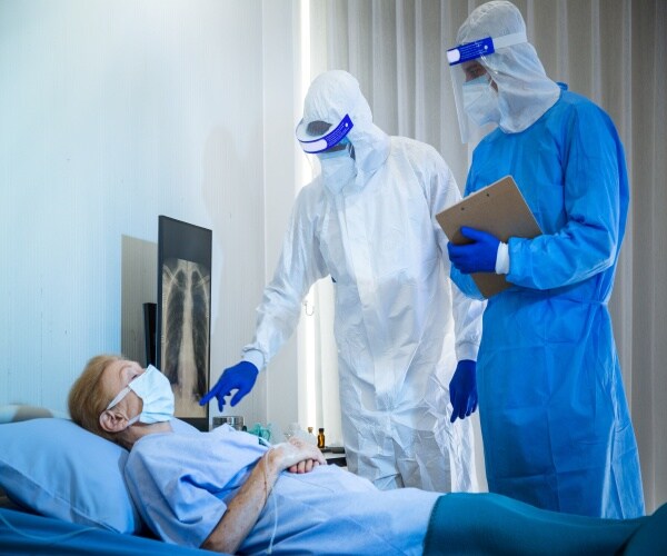 Female patient in hospital bed with two doctors in masks/gowns attending to her