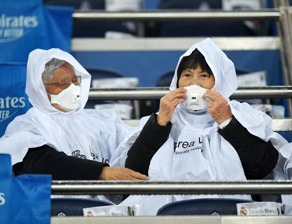 two soccer fans wear face masks and disposable ponchos at a soccer match in madrid spain