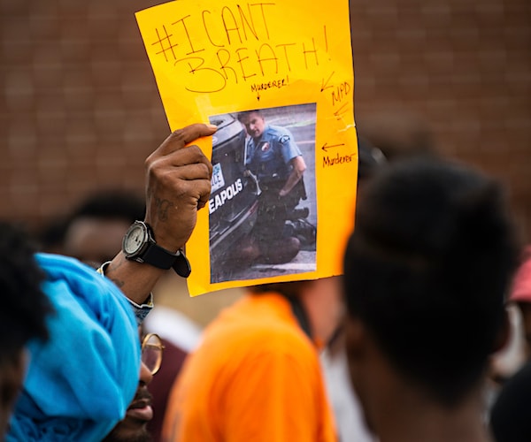 a protester holds a photo of derek chauvin killing george floyd