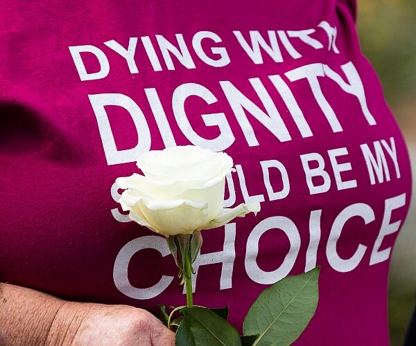 woman holds white rose while wearing tshirt that says dying with dignity should be my choice