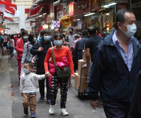 a mother holds her son's hand, both wearing a facemask