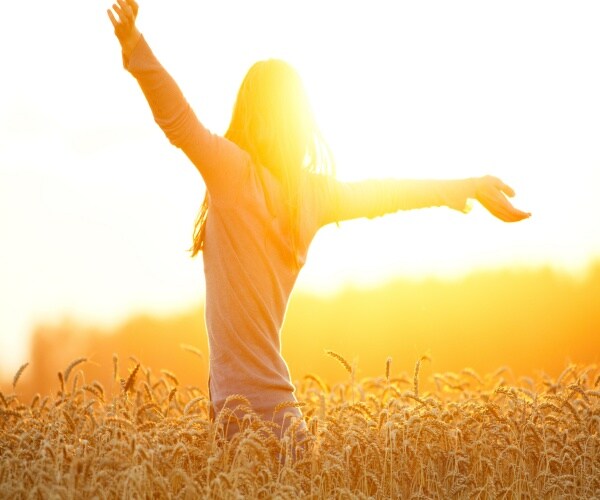 a woman in a field looking toward the sun