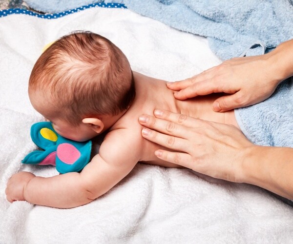 baby on stomach with a person's hand on his or her back