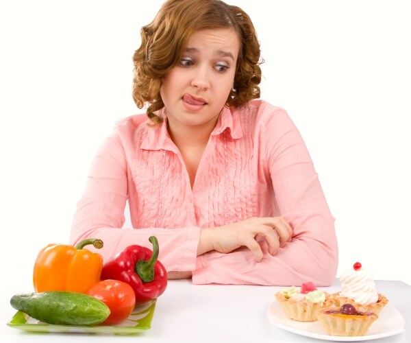 woman looking at a plate of dessert versus the plate of vegetables