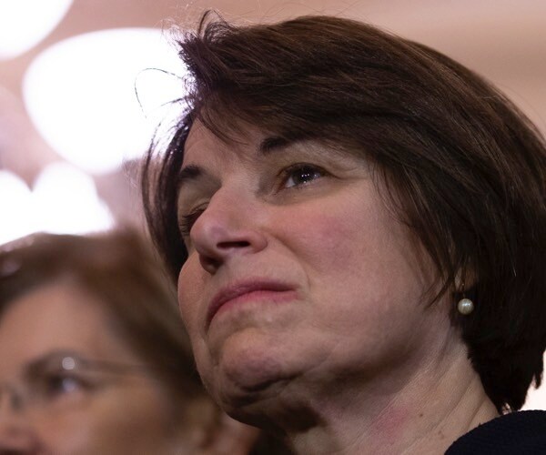 sen. amy klobuchar looks on as senate minority leader chuck schumer speaks to reporters.