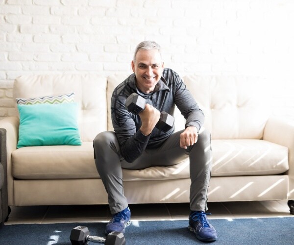 man siting on couch at home doing a bicep curl with a free weight