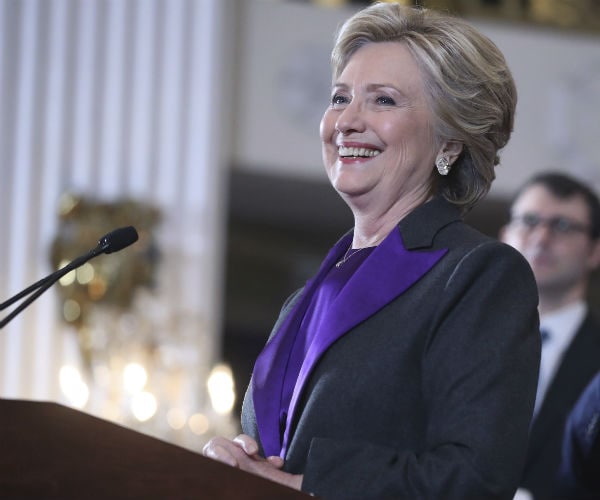 a smiling hillary clinton is shown in a purple suit jacket