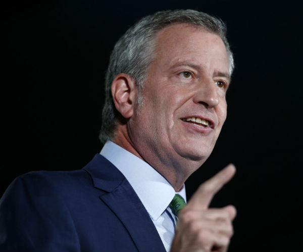 bill de blasio points with his right hand as he smiles smugly during a news conference