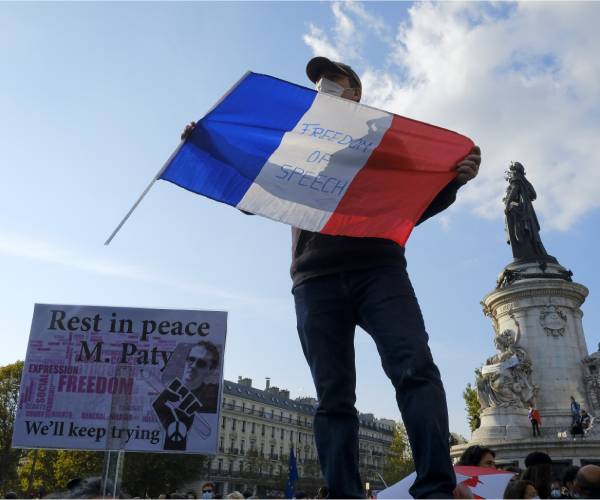 a man stands among protesters holding the french flag with freedom of speech written on it